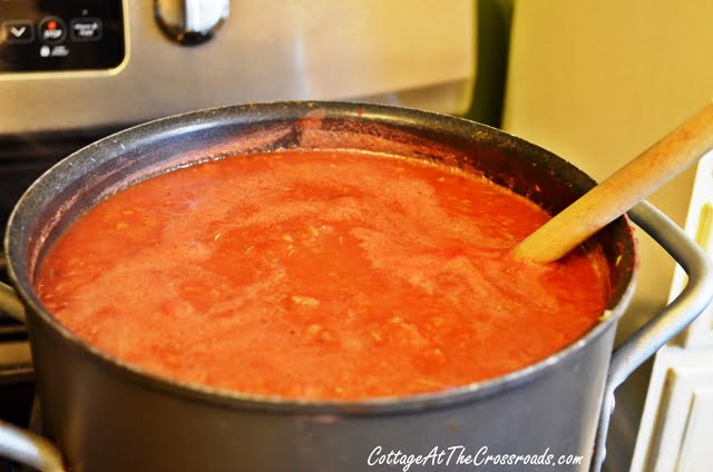 Homemade spaghetti sauce simmering on stove in large pot with wood spoon.