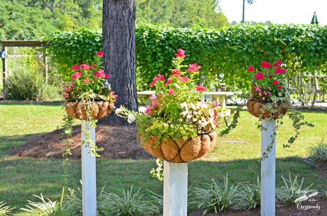 Flower baskets mounted on wooden posts | cottage at the crossroads