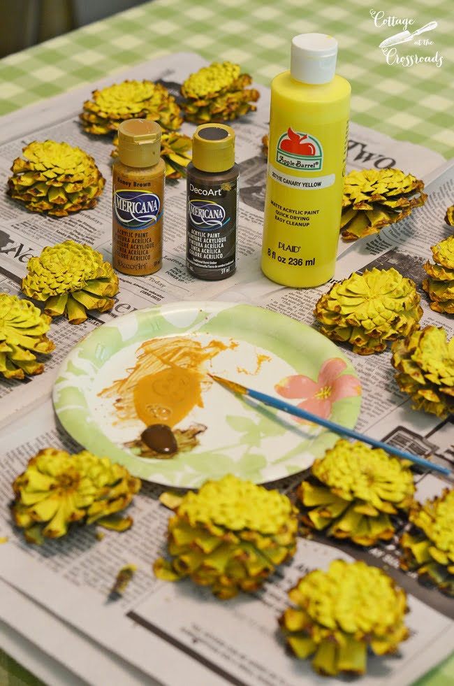 Painting cut pine cones to look like a pineapple