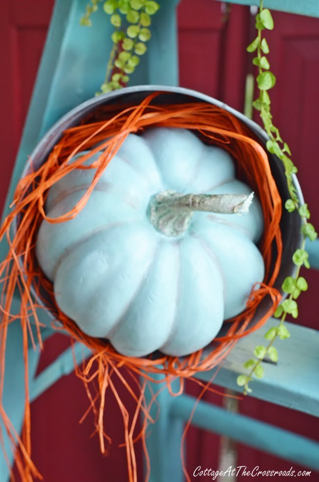 Aqua faux pumpkin on a porch decorated for fall