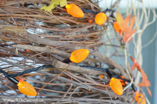 Orange lights on a handmade grapevine tree used in decorating an autumn porch