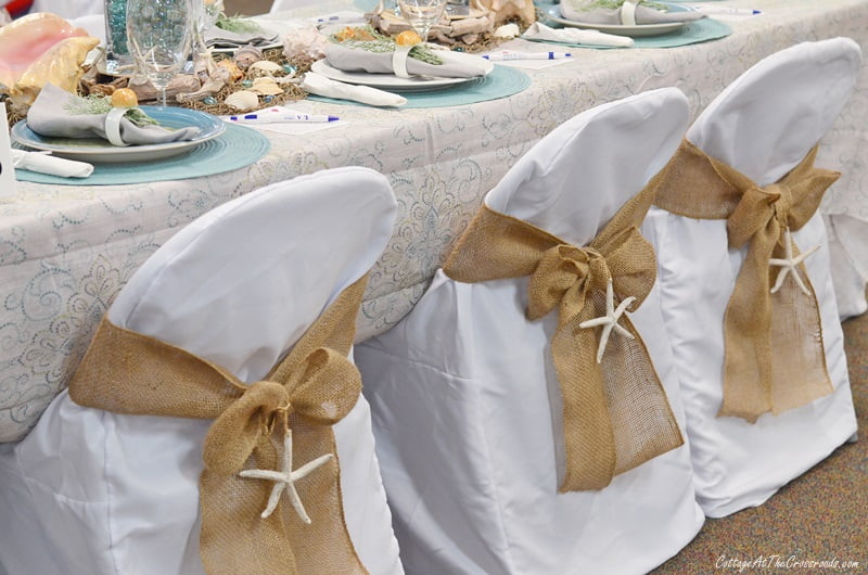 A coastal themed tablescape with chair covers decorated with starfish