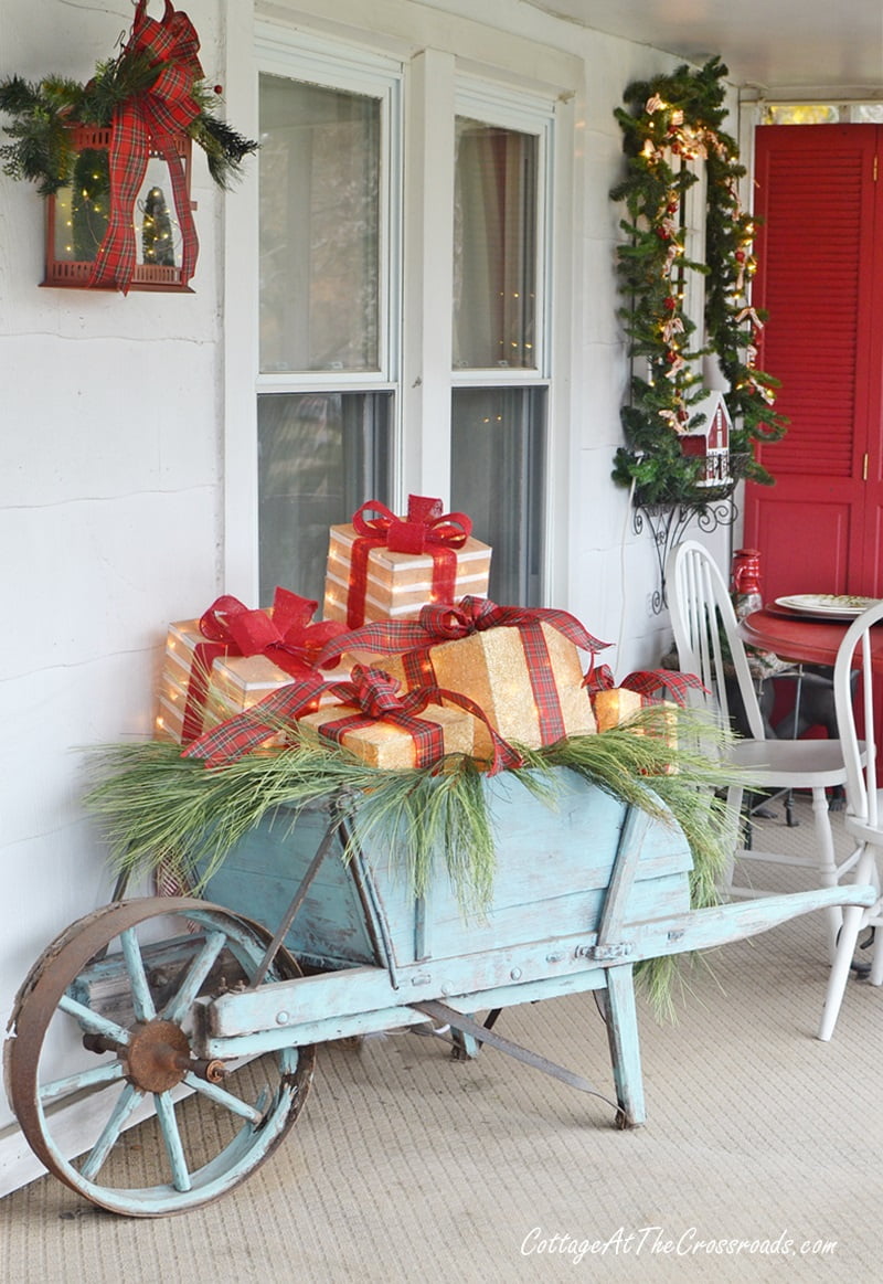 Wheelbarrow filled with lighted boxes on a christmas front porch