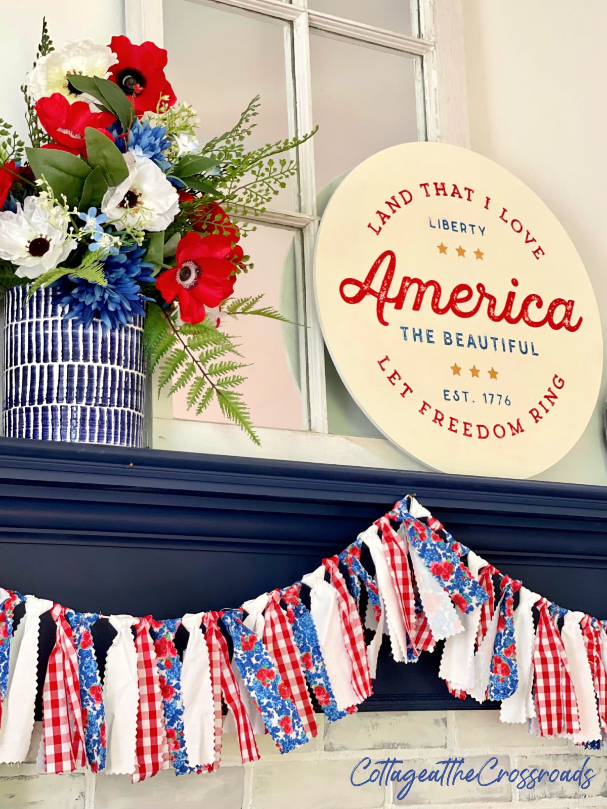 Round patriotic sign, floral decorations, and garland on a navy mantel