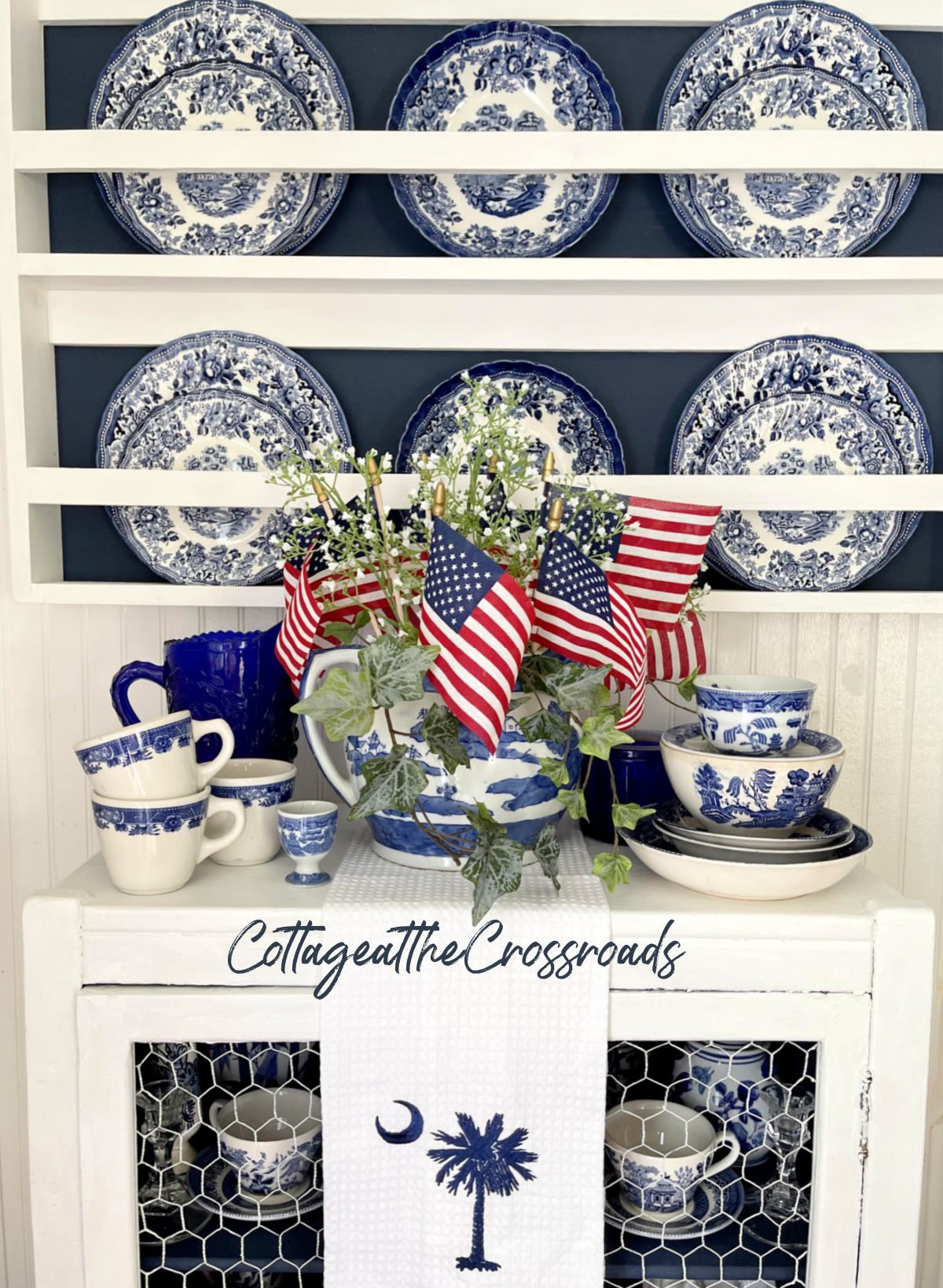 Blue and white china displayed in a wooden plate rack with flags tucked down inside a jar