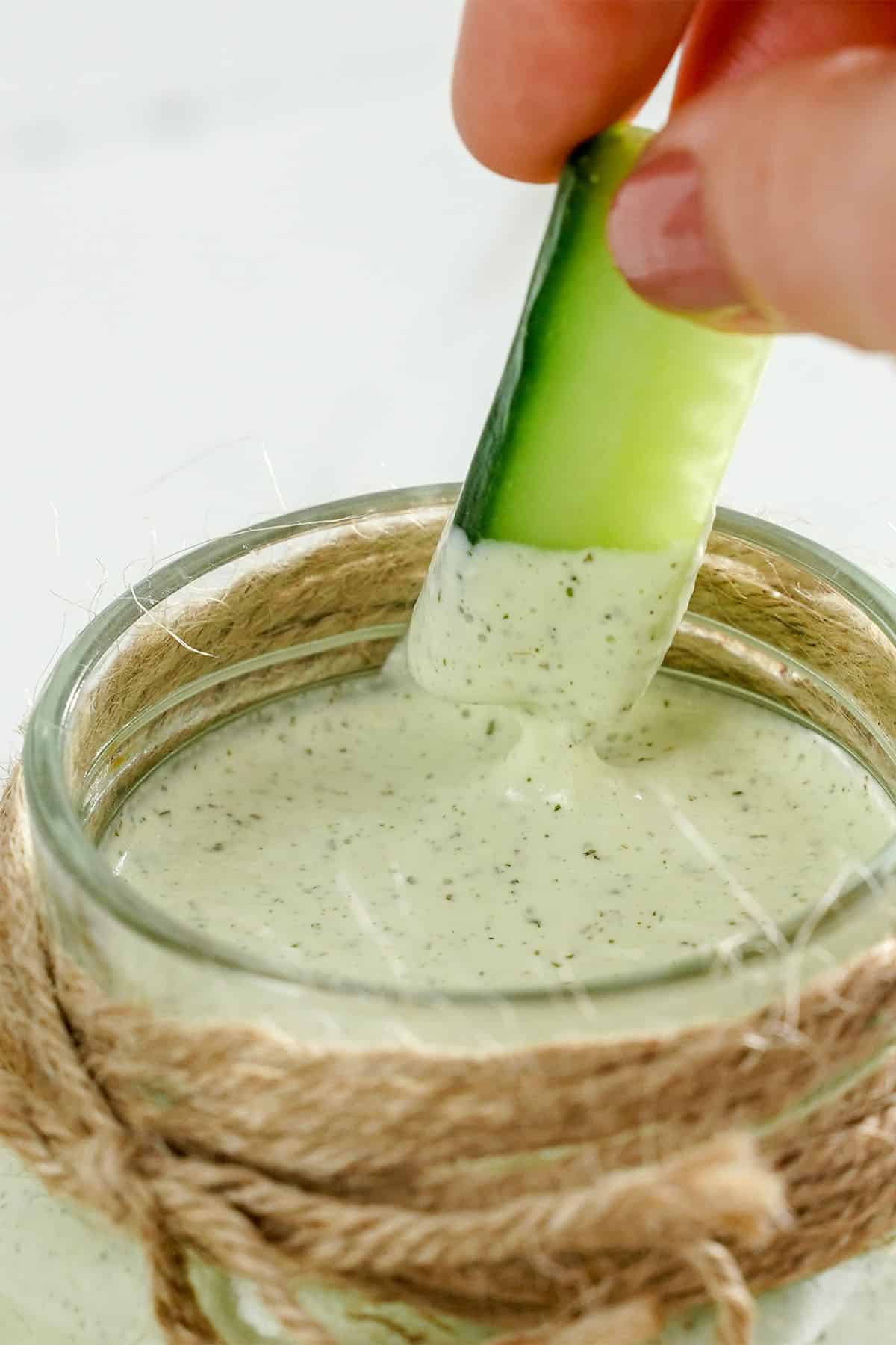 Cucumber being dipped into homemade cucumber ranch dressing