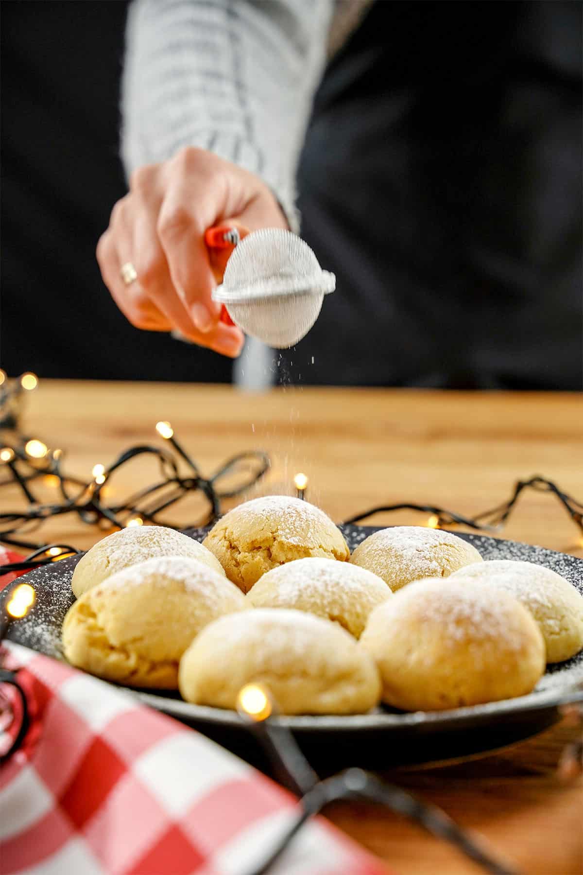 Powdered sugar being sprinkled over snowball cookies