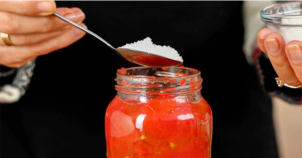 Salt being added to a jar of homemade canned tomatoes
