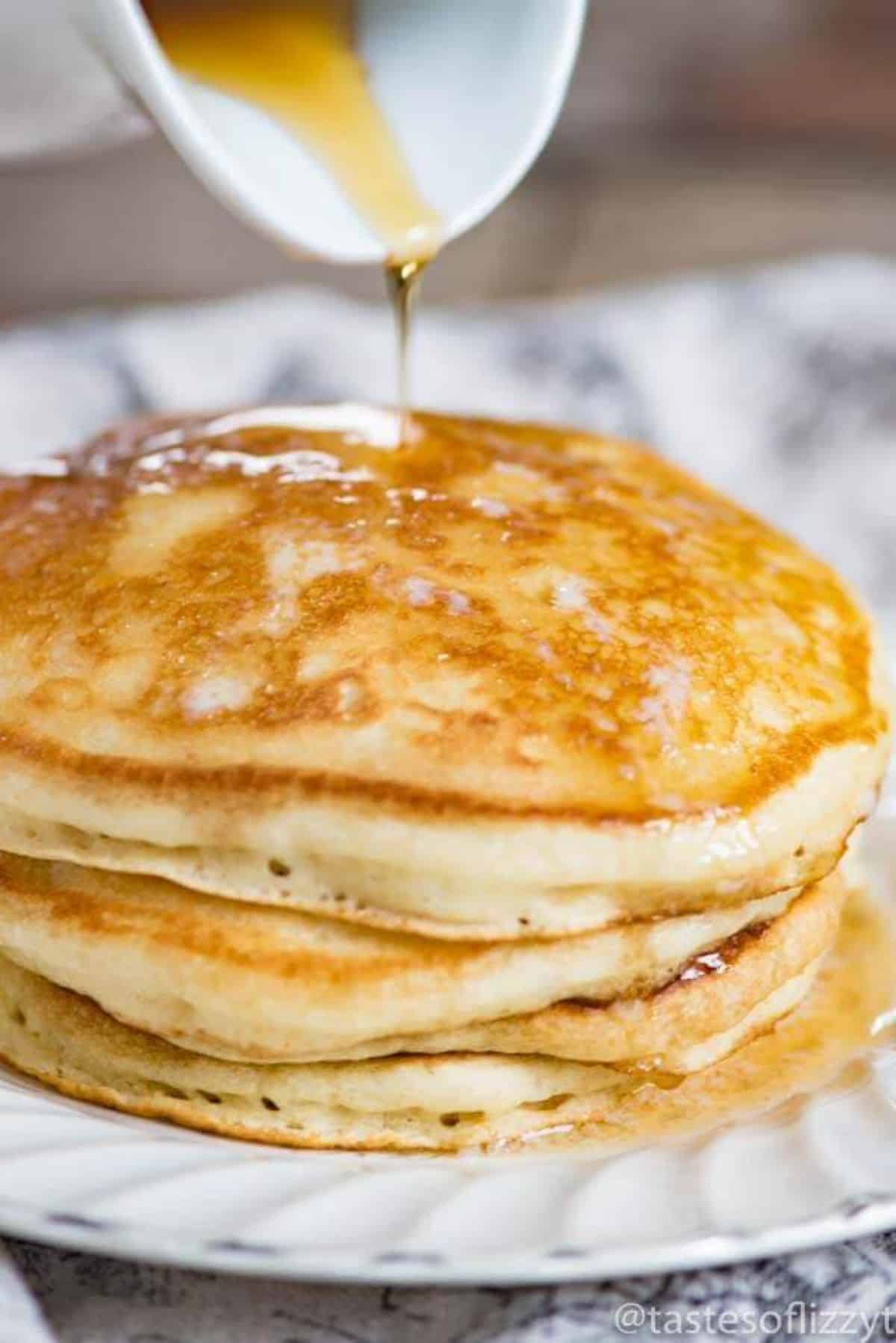 Sourdough pancakes on a white plate poured with maple syrup.