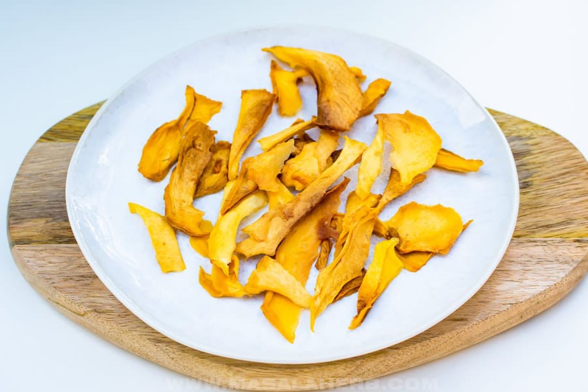 Sweet dehydrated mangos on a white plate on a wooden tray.