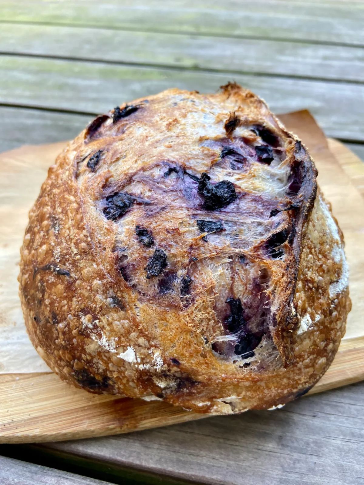 A loaf of blueberry sourdough bread on a wooden cutting board.