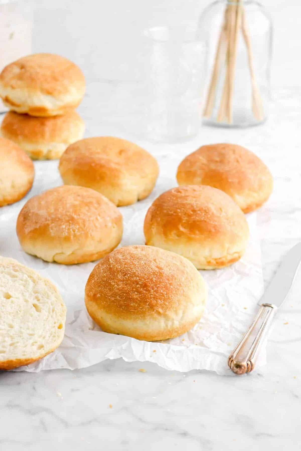 Sourdough hamburger buns on parchment paper with a knife.