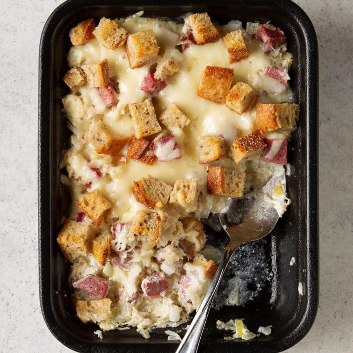 Creamy ruben in a black casserole with a spoon.