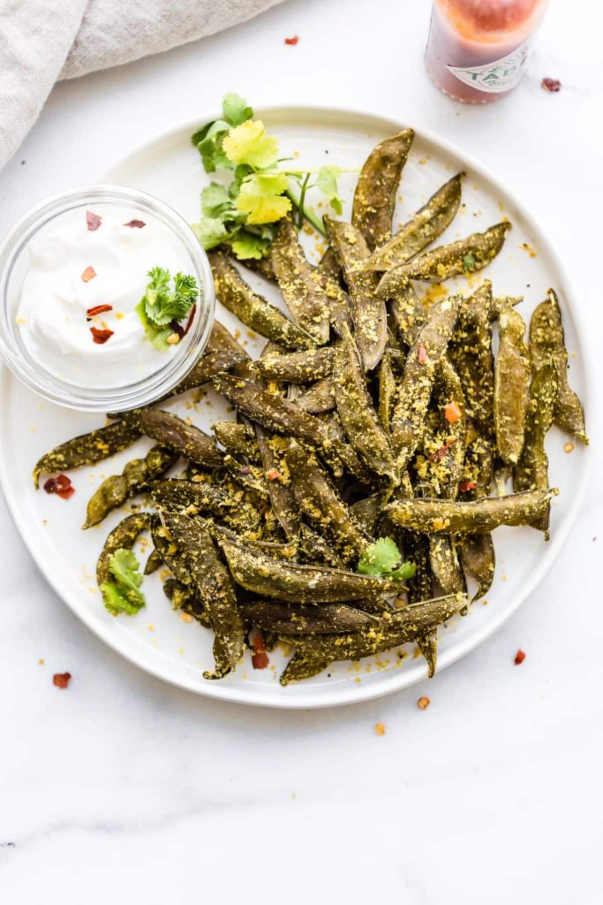 Homemade snap peas chips with a bowl of dip on a white tray.