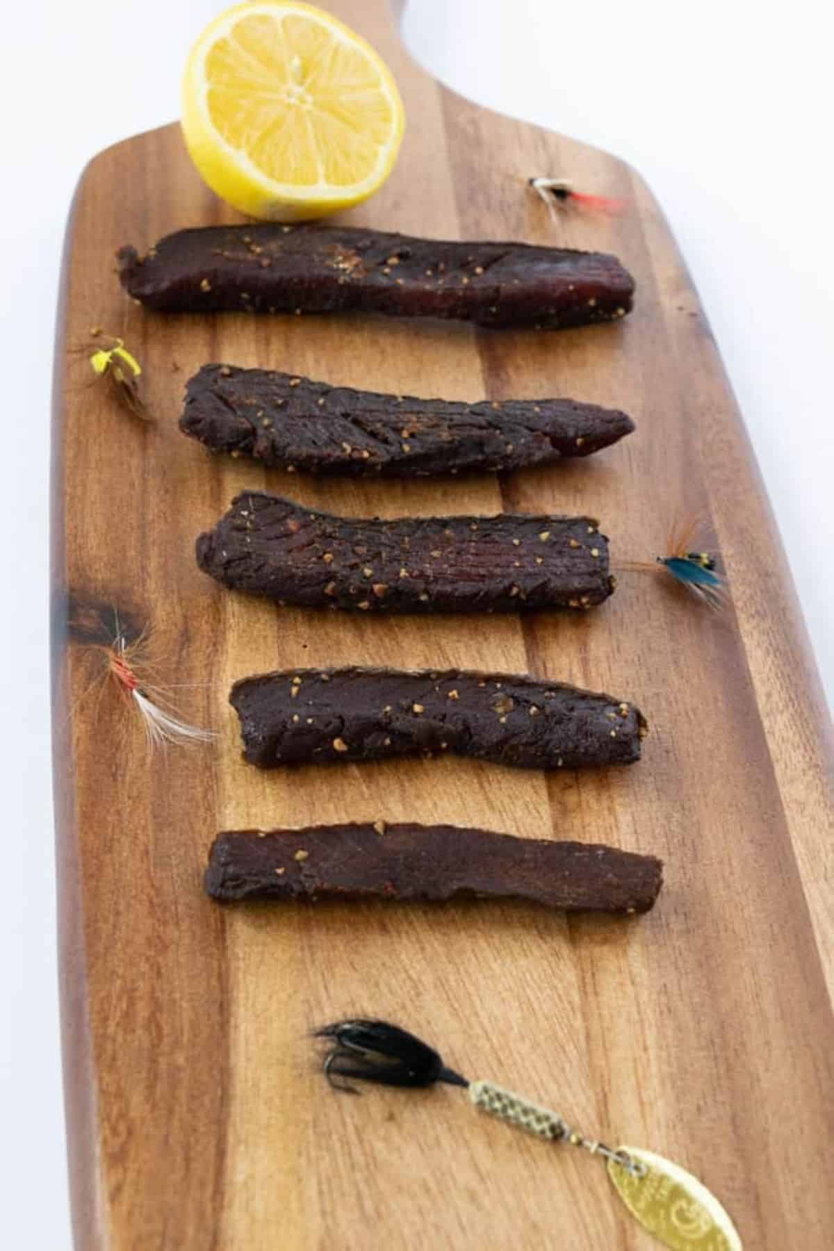 Salmon jerky with a halve of lemon on a wooden cutting board.