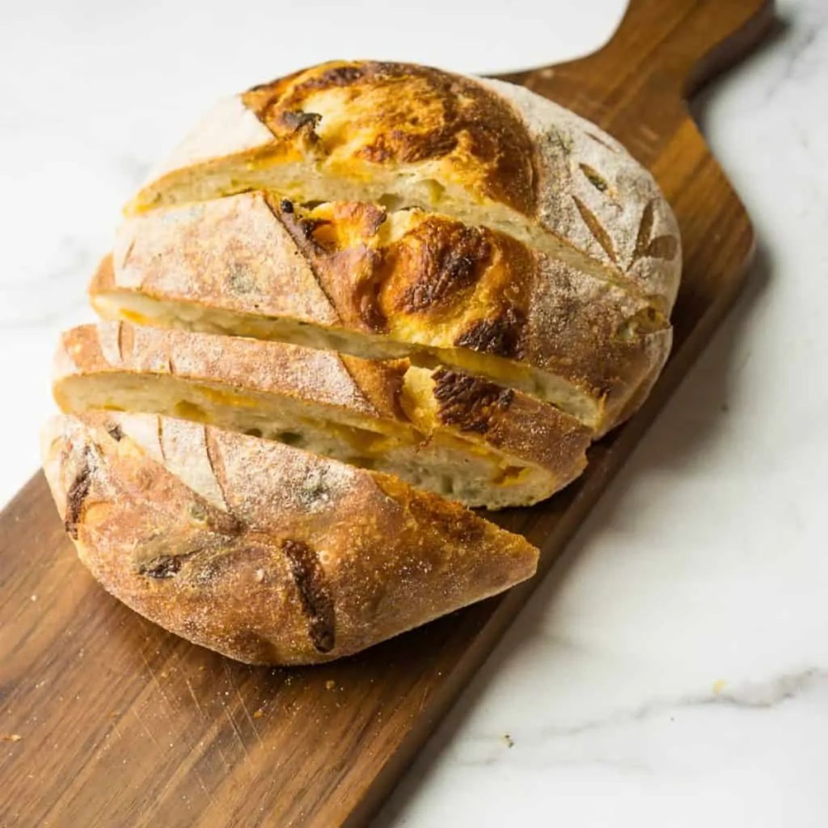 A loaf of jalapeno cheddar sourdough bread on a wooden cutting board.