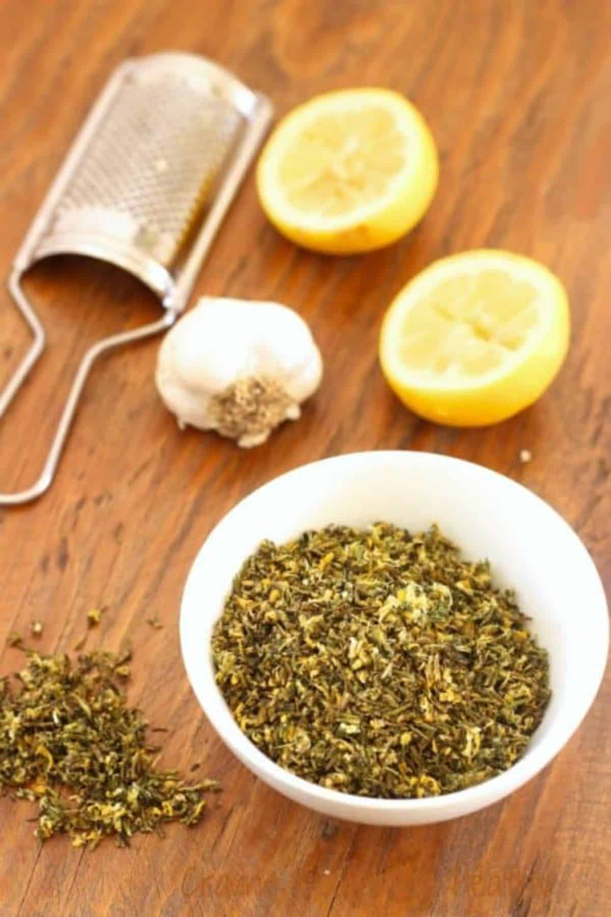 Rosemary, thyme, lemon, and garlic herb mix in a white bowl.