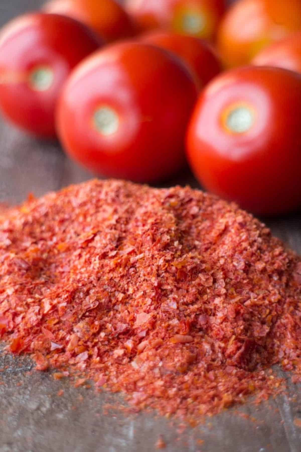 A pile of tomato powder with while tomatoes in the background.