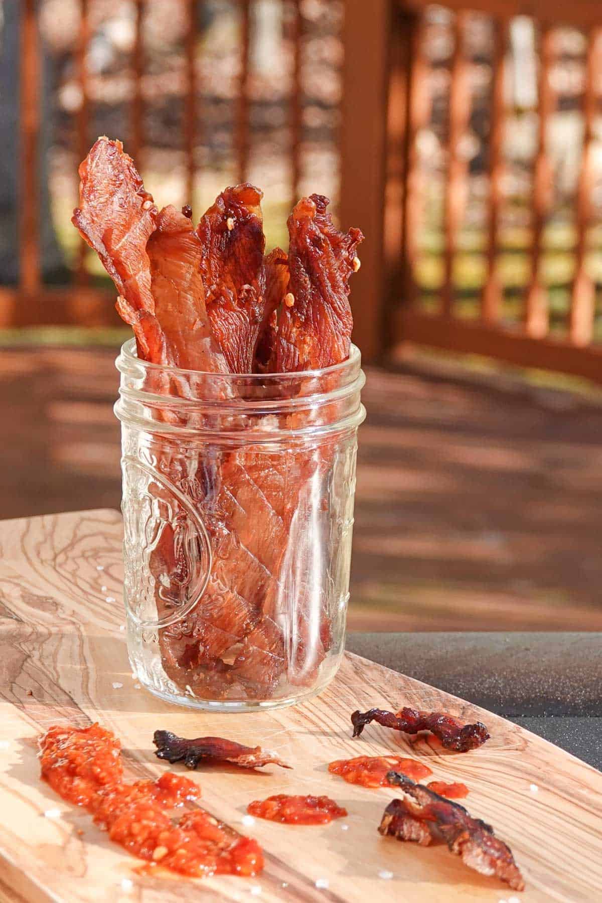 Chicken jerky in a glass jar on a wooden board.