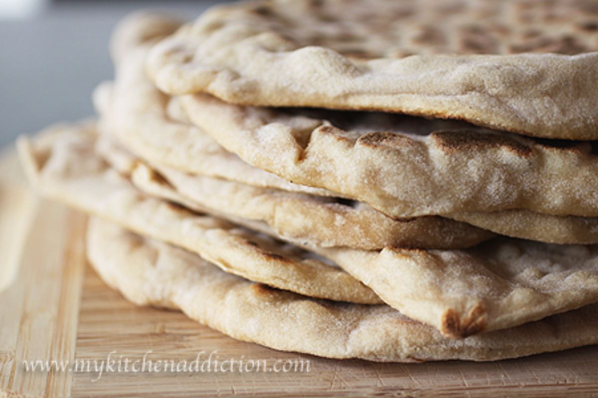 A pile of sourdough naan on a wooden cutting board.