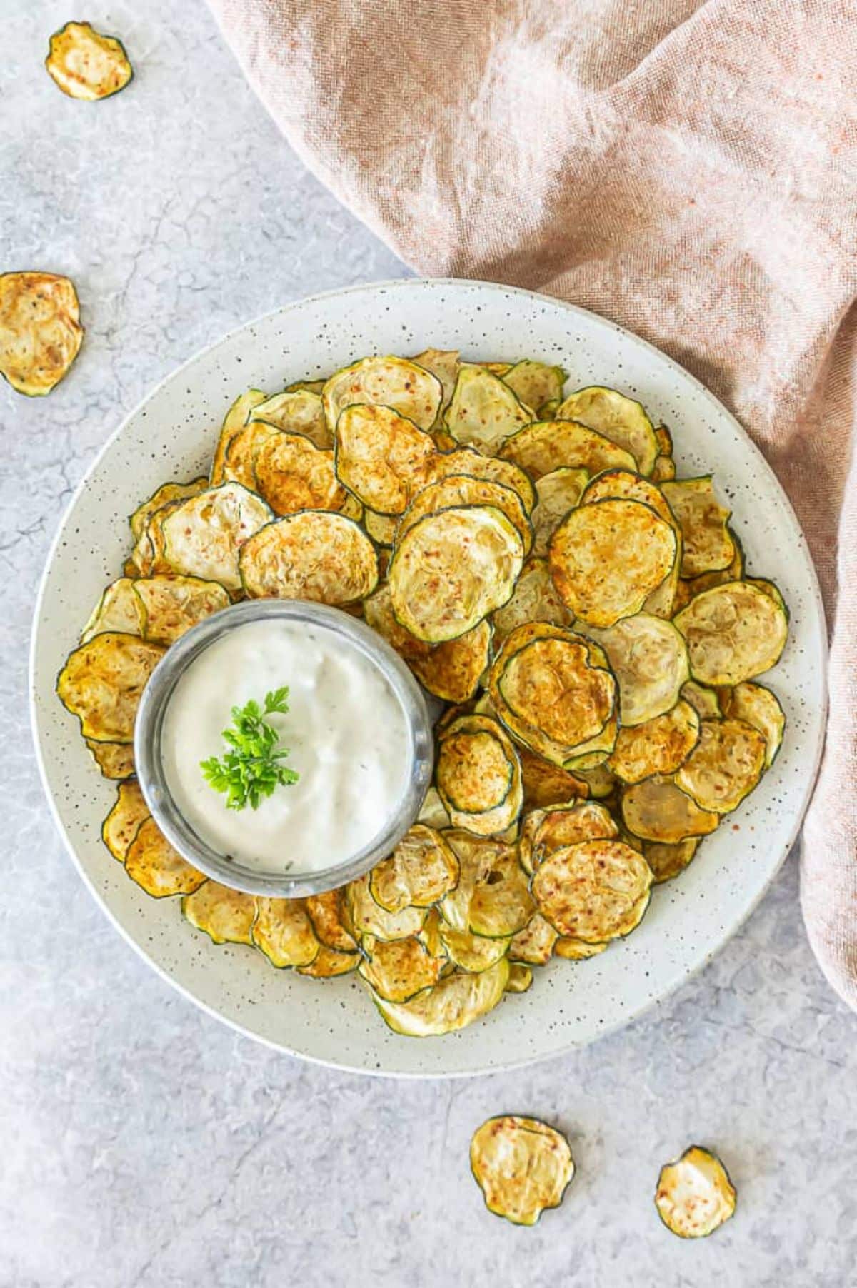 Crispy zucchini chips with a bowl of dip on a plate.