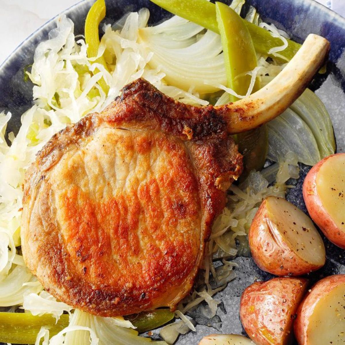 Pork chops with sauerkraut and potatoes on a blue plate.