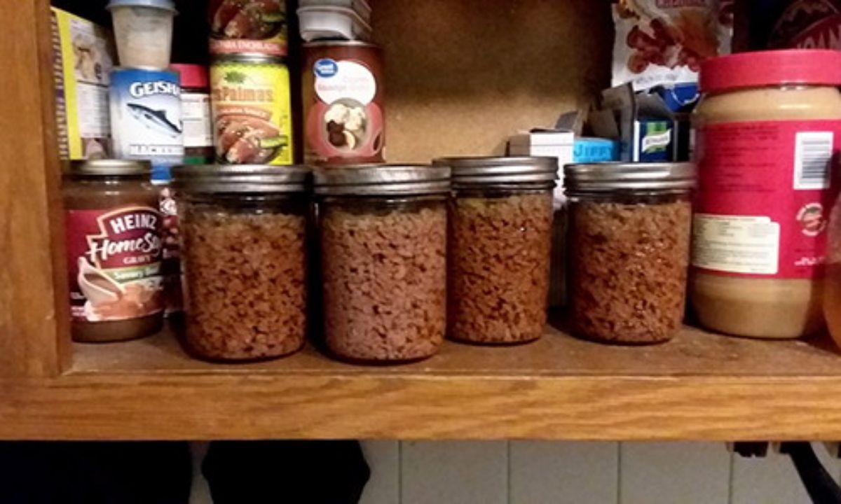 Canned hamburger meat in glass jars on a shelf.