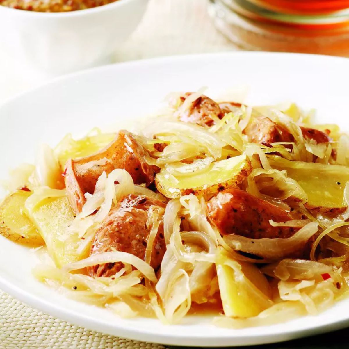 Chicken sausage with potatoes & sauerkraut on a white plate.