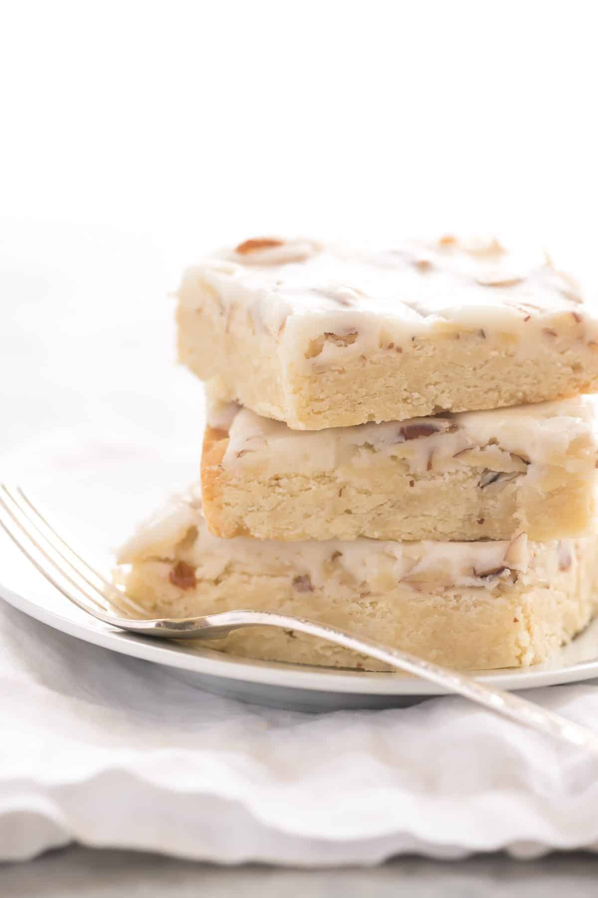 A pile of almond shortbread bars on a white plate with a fork.