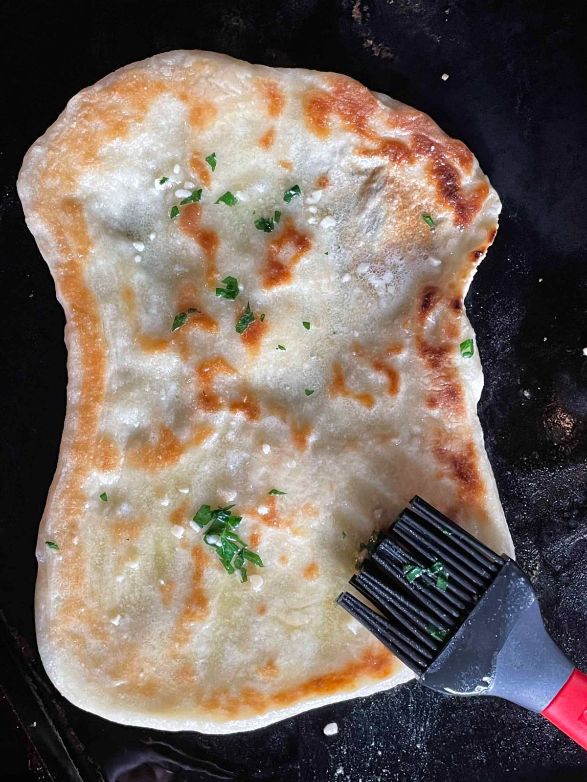 Garlic naan bread on a black pan.