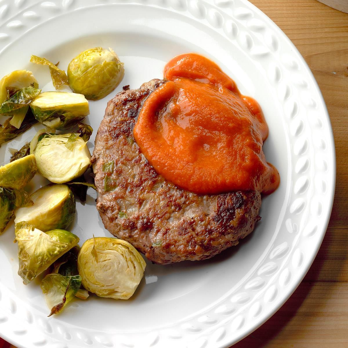 Meat and potato patties with brussels sprouts on a white plate.