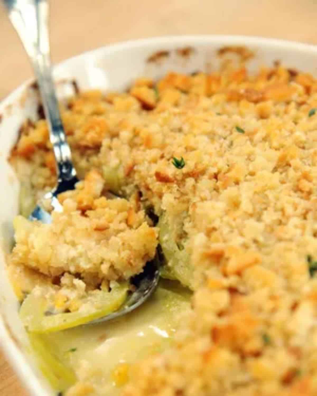 Scalloped green tomatoes dish in a white casserole with a spoon.