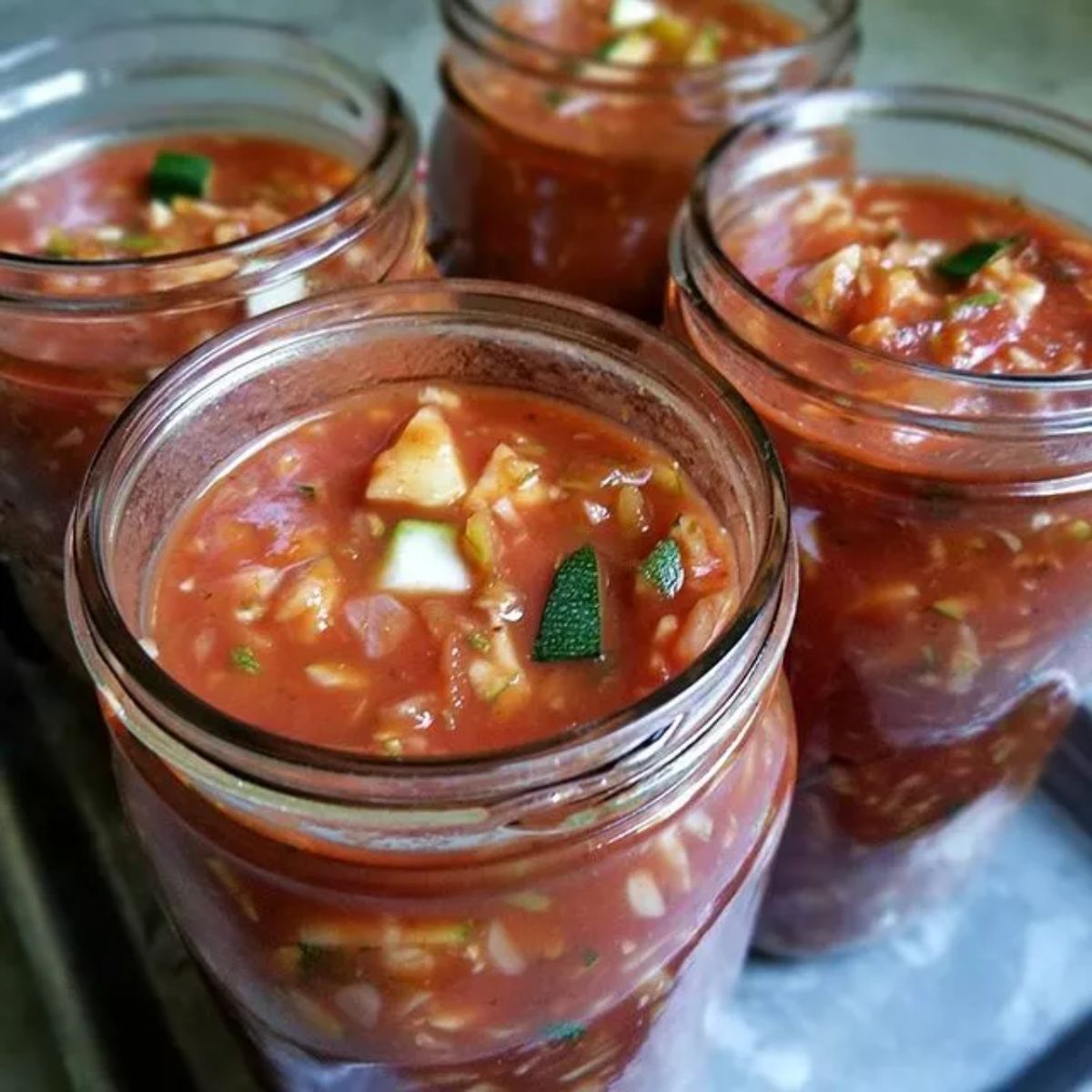 Homemade zucchini tomato sauce in four glass jars.