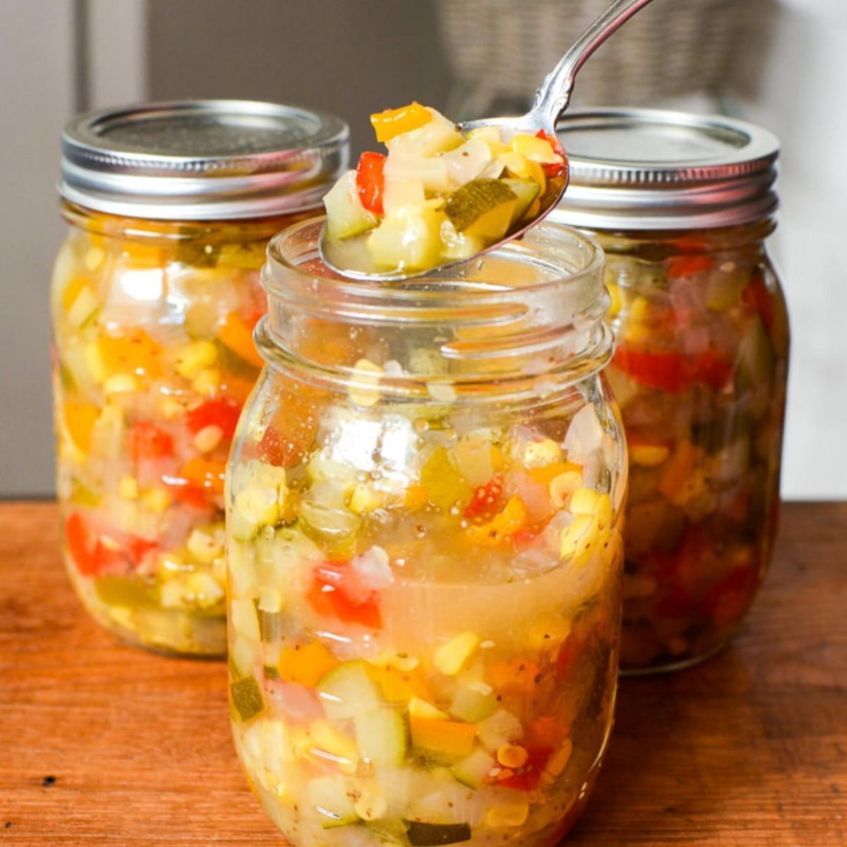 Zucchini corn relish in three glass jars.
