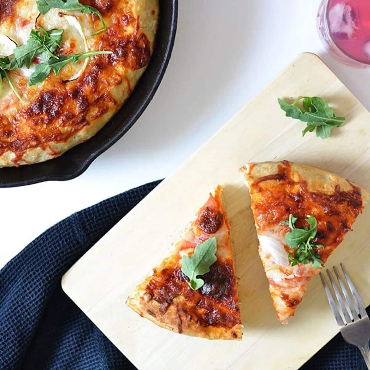 Two slices of cast iron pizza on a wooden cutting board.