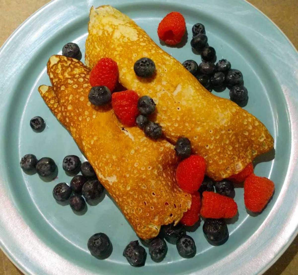 Crepe with ripe fruits on a blue plate.