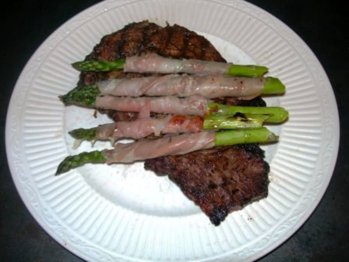 Delicious grilled asparagus wrapped with prosciutto on a white plate.