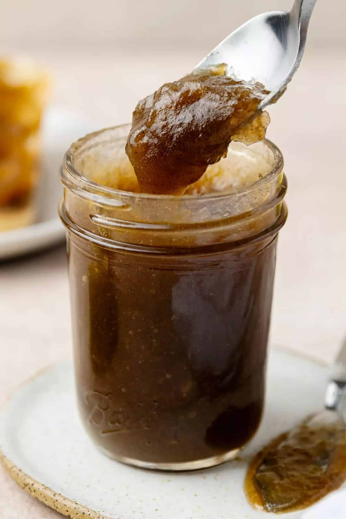 Classic apple butter in a glass jar picked by a spoon.