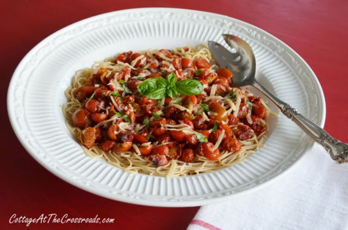 Roasted balsamic cherry tomatoes with angel hair pasta on a white plate with a spoon.