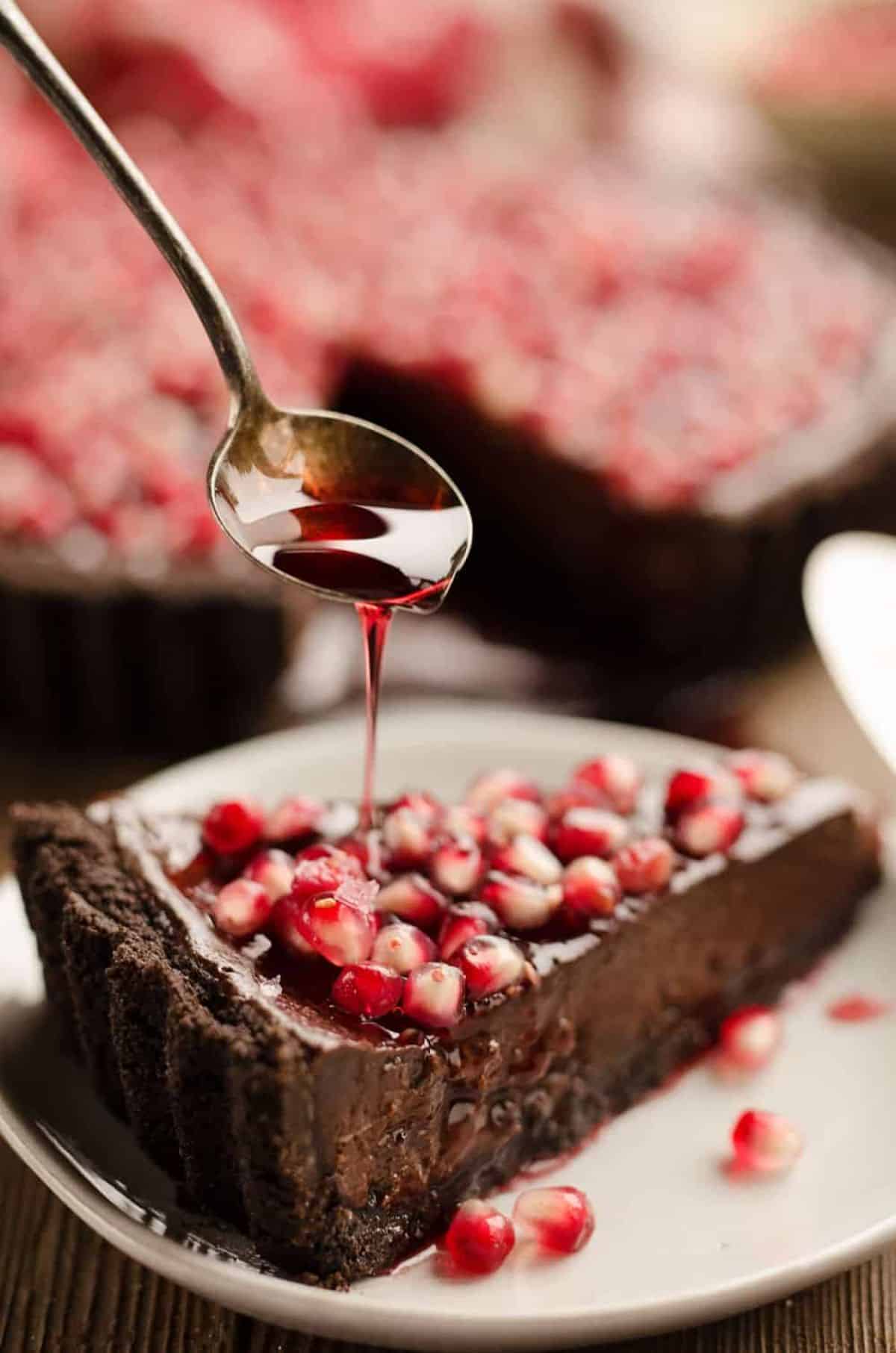 A piece of salted dark chocolate tart on a white plate poured with pomegranate juice.