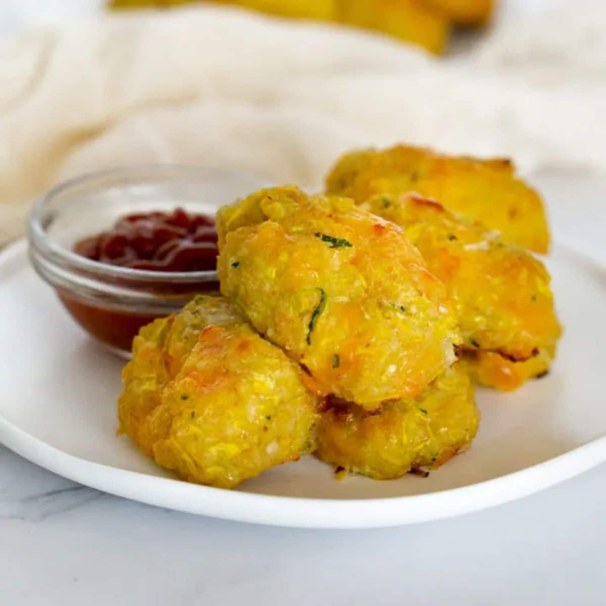 Yellow squash tots with garlicky yogurt dip on a white plate.