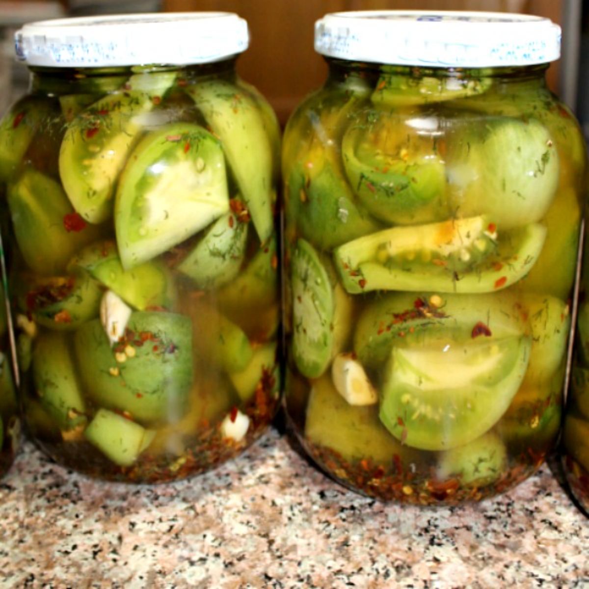 Spiced pickled green tomatoes in two glass jars.