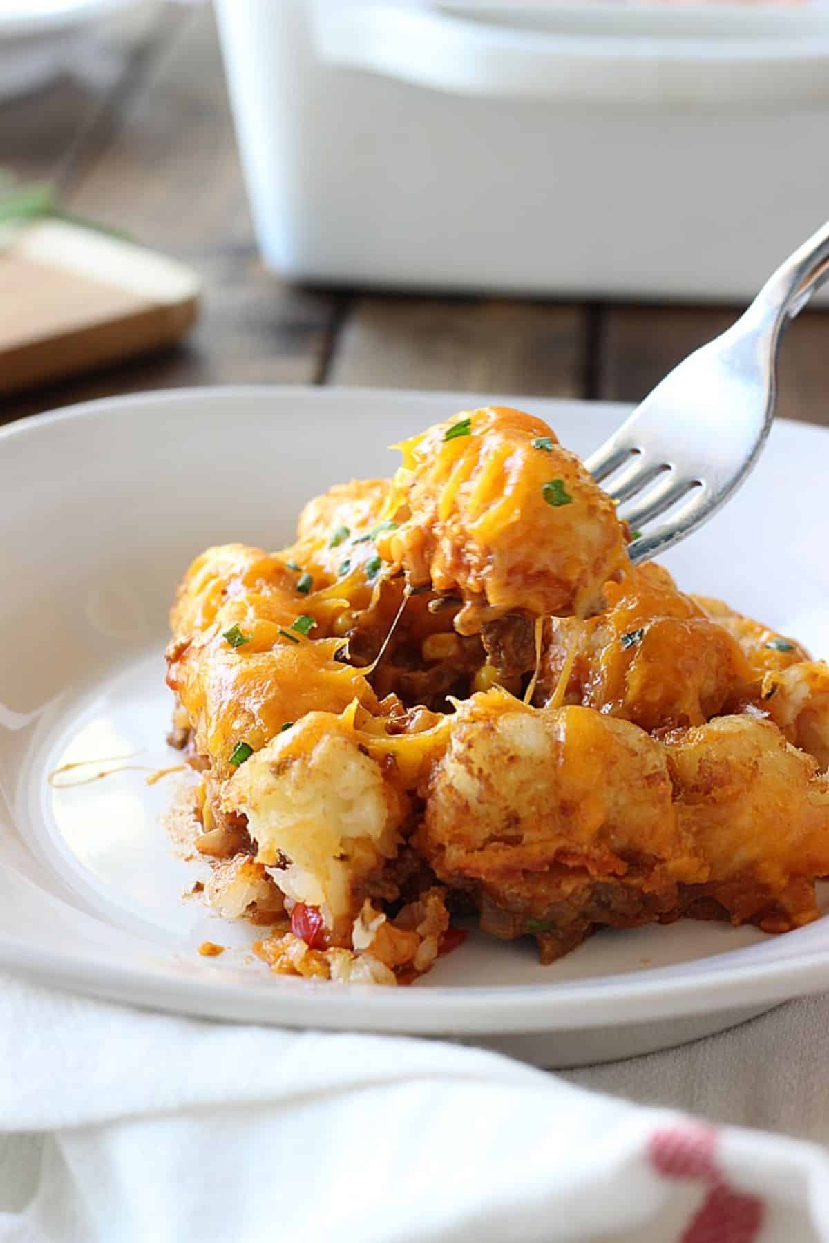 Deliicous sloppy joe tater tots on a white plate picked with a fork.