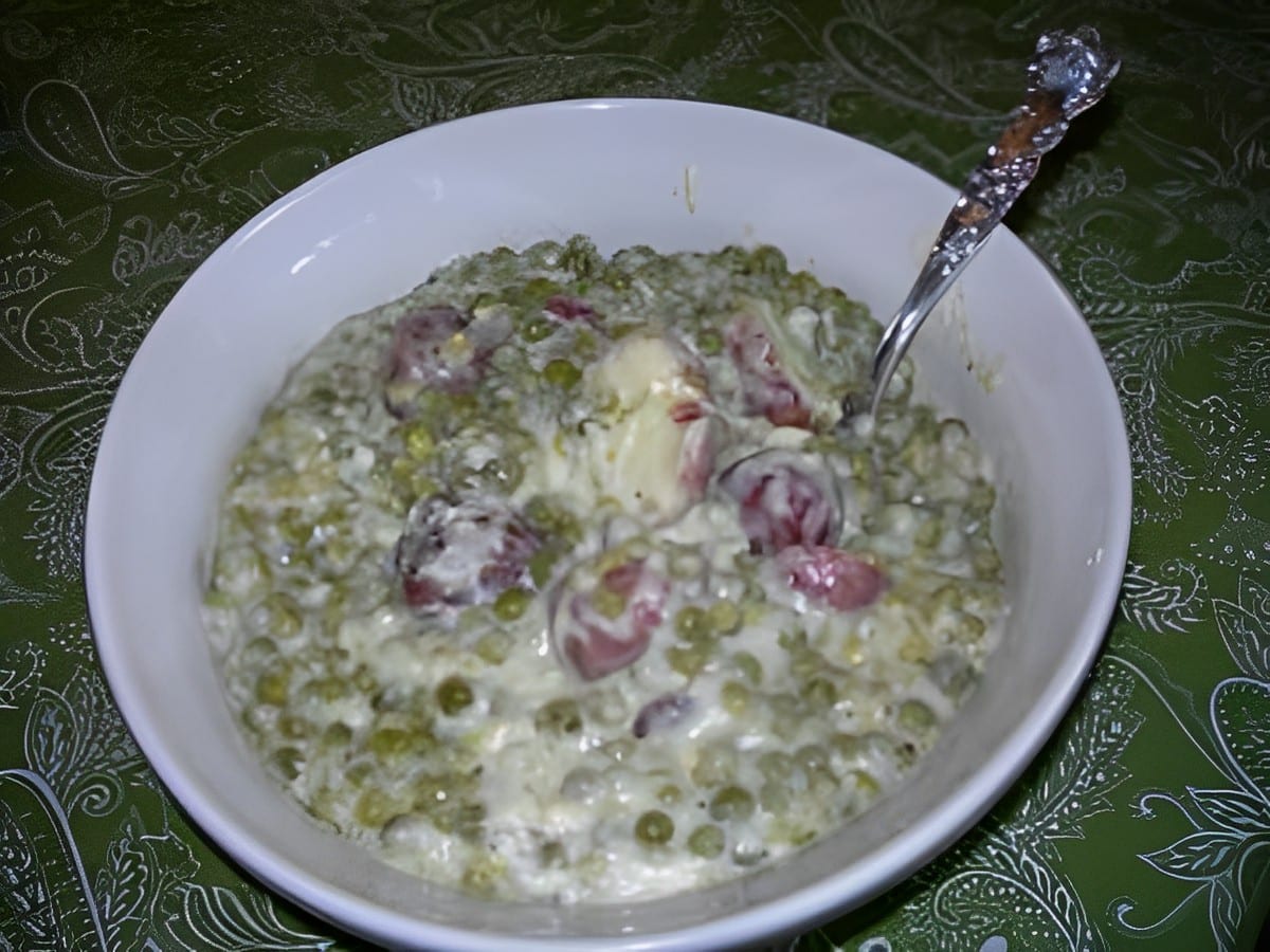 Creamed garden peas and new potatoes in a white bowl with a spoon.