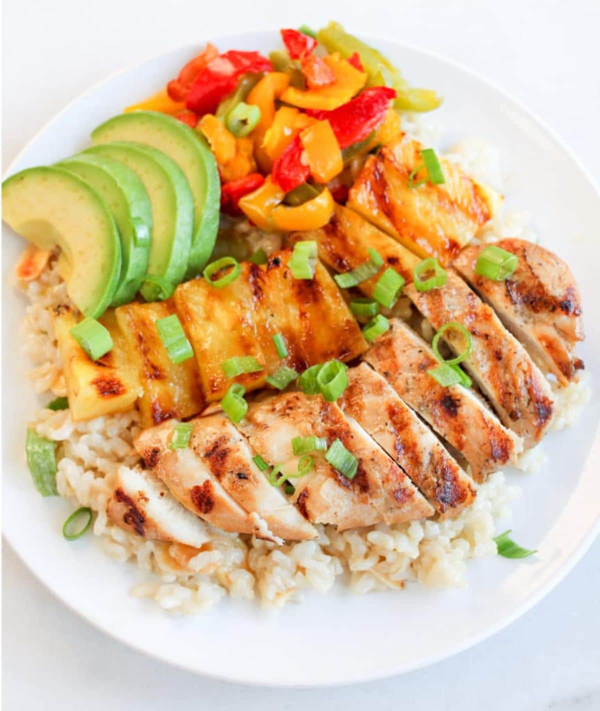 Healthy grilled hawaiian chicken with veggies and rice on a white plate.