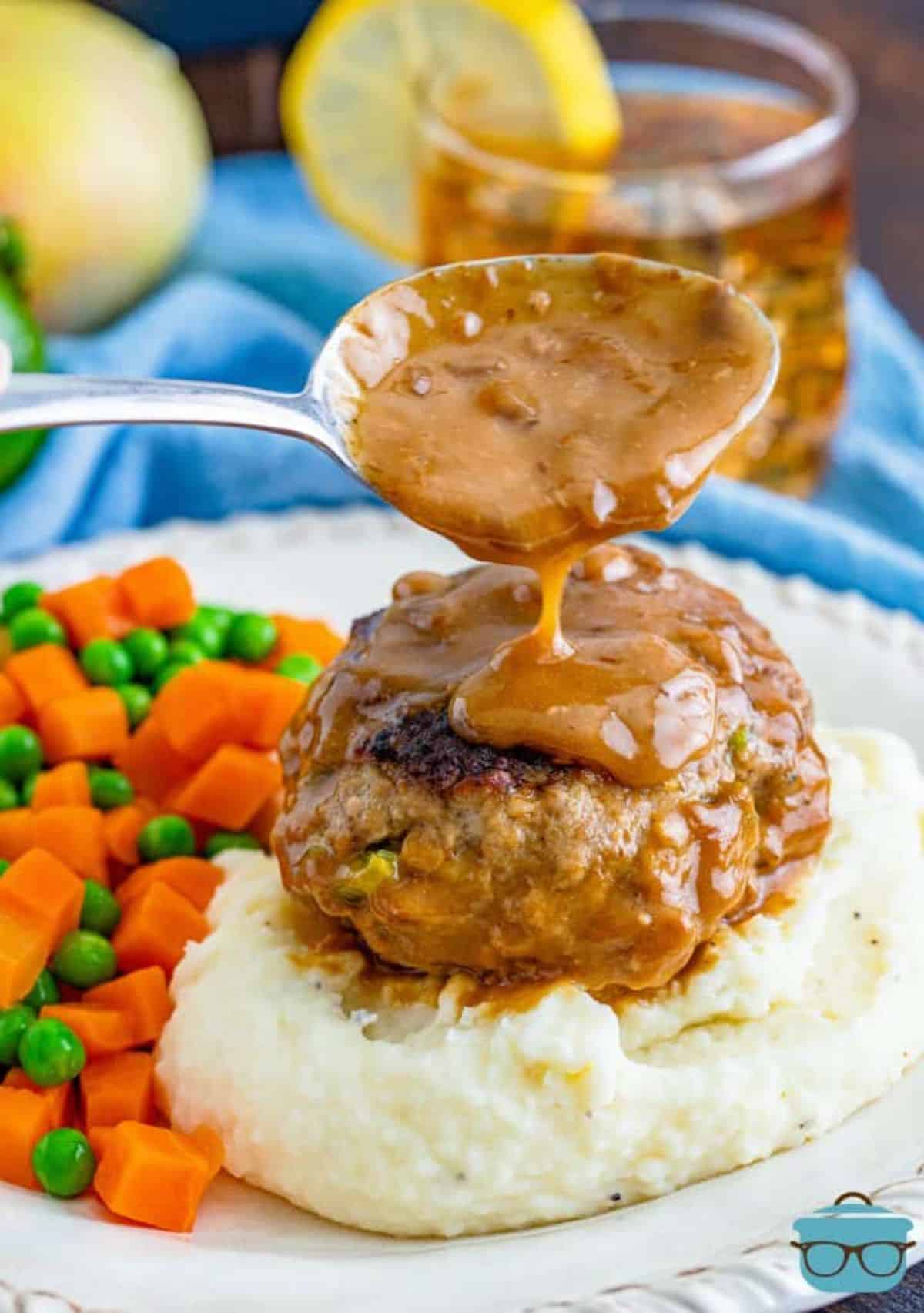 Hamburger steak poured with gravy with veggies on a white plate.