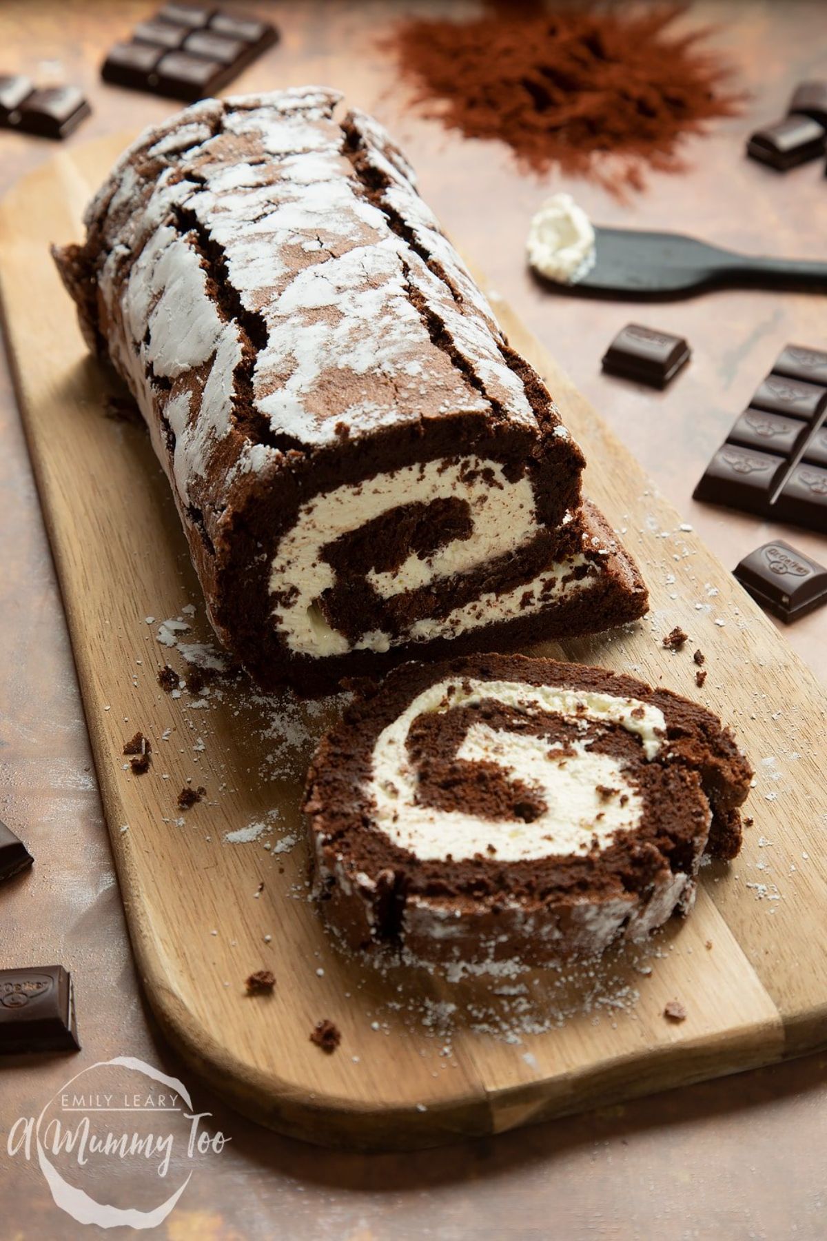 Scrumptious chocolate roulade partially sliced on a wooden cutting board.