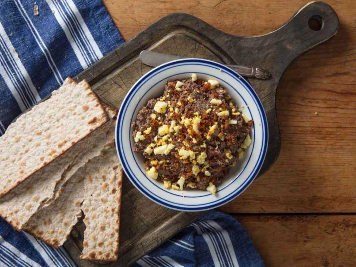 Deliicous chopped liver in a bowl with pieces of bread on a wooden cutting board.