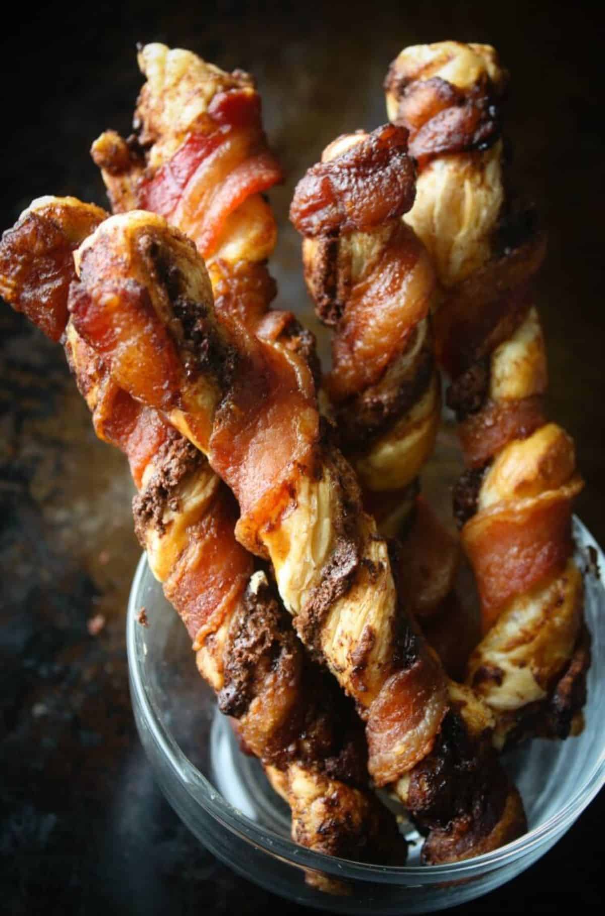 Crunchy nutella bacon puff pastry twists in a glass cup.