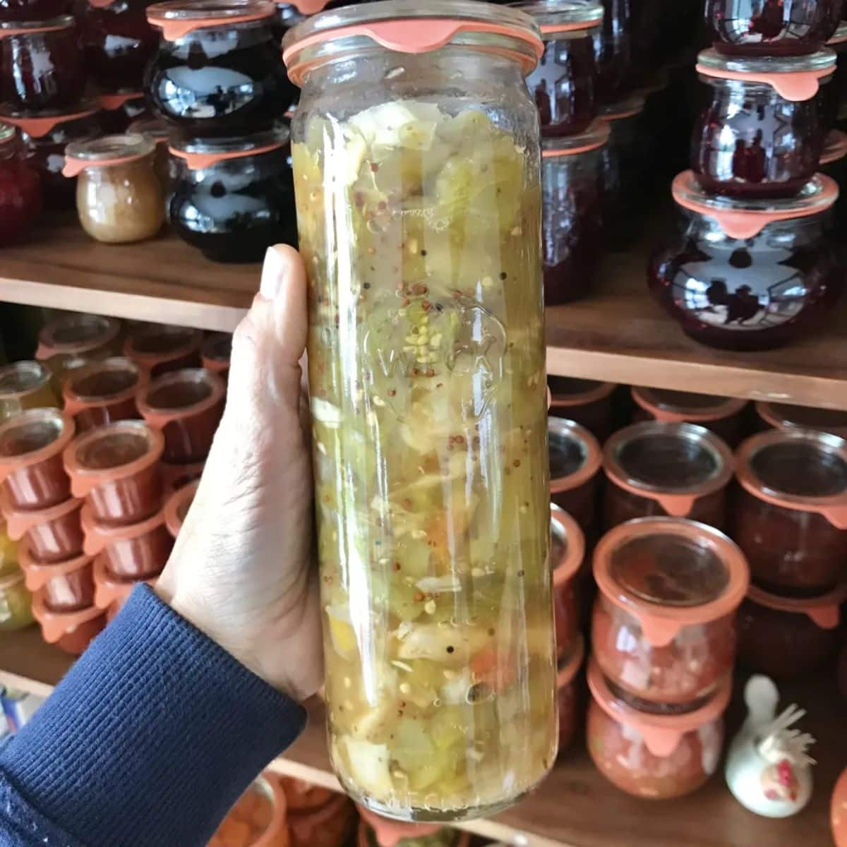 Green tomato piccalilli canned in a glass jar held by hand.